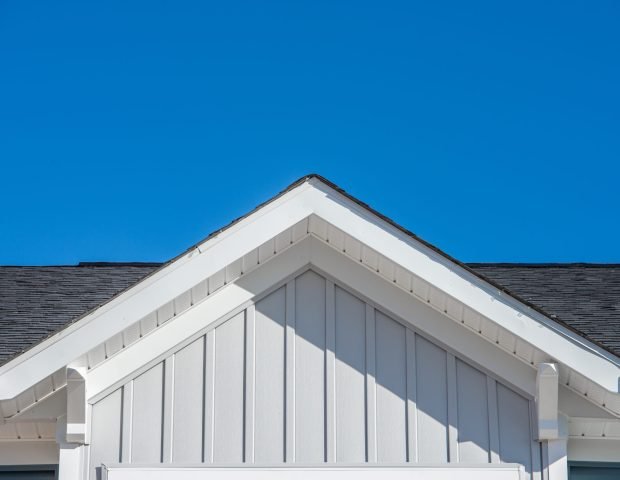 Gable roof with white fascia, gray vertical vinyl lap siding blue sky background